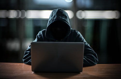 Hacker in hoodie sitting in front of laptop