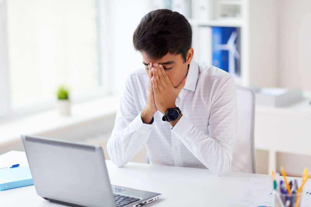 Stressed businessman covering face with hands sitting in front of laptop