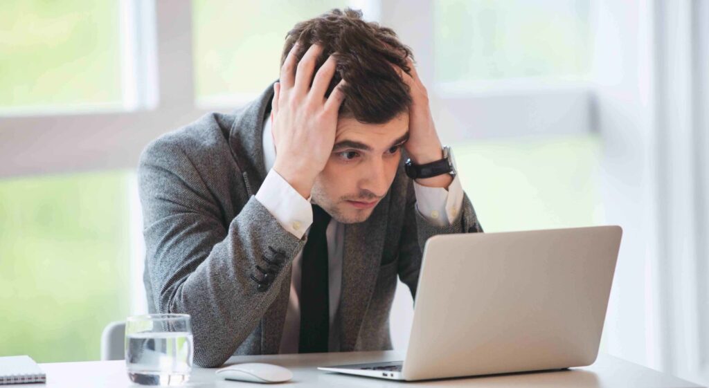 Young businessman stressed out with hands on head looking at laptop