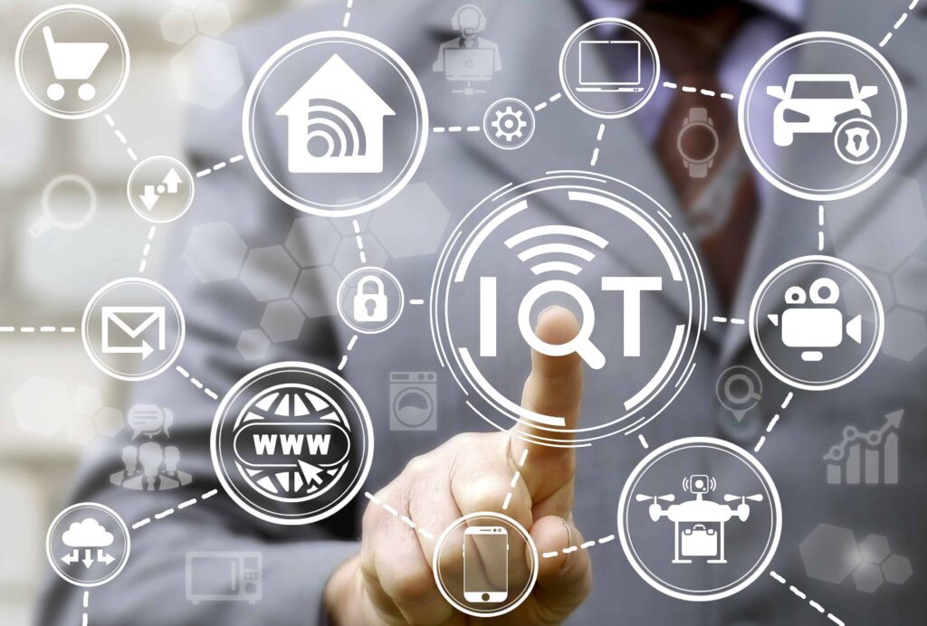Businessman Presses Iot Button On Virtual Screen On Background Of Network Smart House Devices Car Drone Computer. Internet Of Things Business Search Concept.