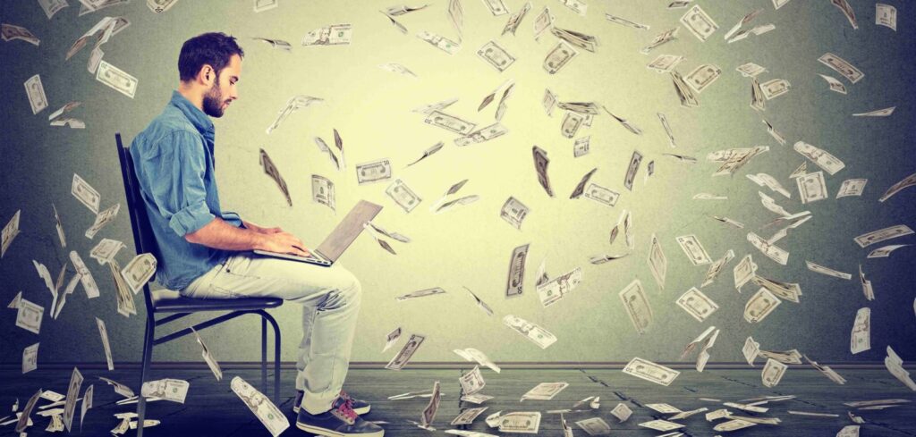 Young man using a laptop building online business making money dollar bills cash falling down. Money rain beginner IT entrepreneur success economy concept