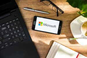 Samsung smartphone on desk next to laptop. phone screen displays the Microsoft logo